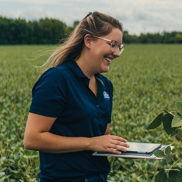 Courtney Courville standing in a field of soy with a tablet speaking with a farmer.