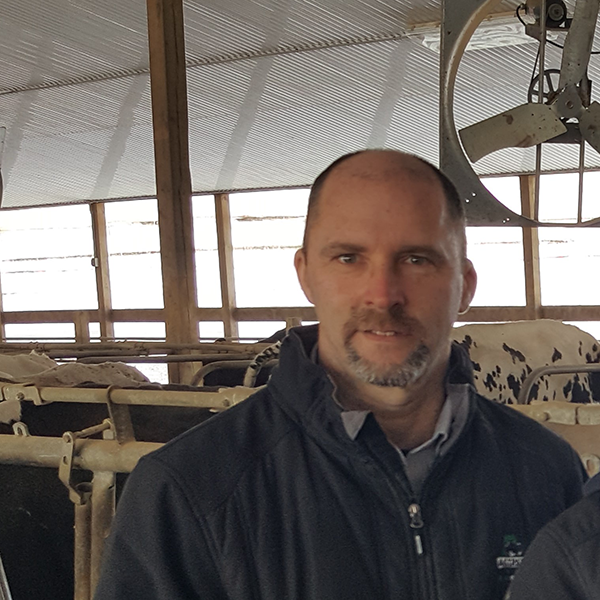 A headshot of Alain Bouvrette standing in front of a comical photo of a cow.